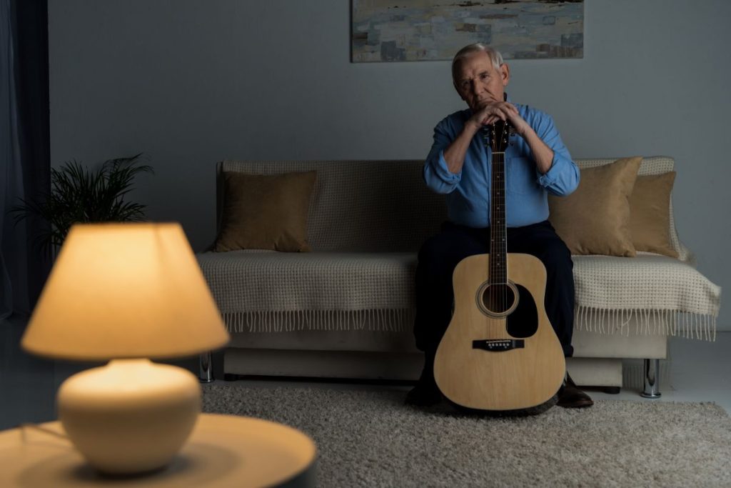 Senior confident man holds acoustic guitar while sitting on sofa in room