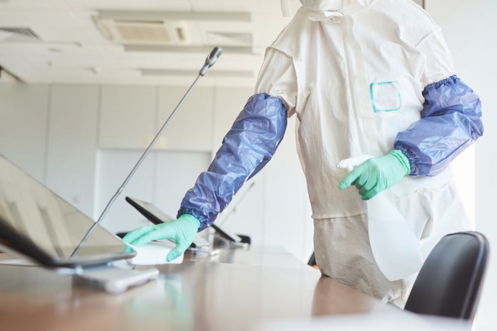 Cropped portrait of sanitation worker wearing hazmat suit cleaning and disinfecting conference room in office, copy space