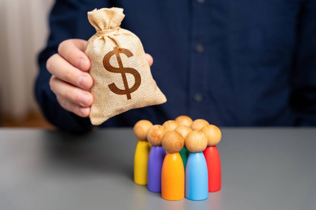 Businessman holding dollar money bag over group of people figurines. Allocation of budget money for social projects. Preferential loans for entrepreneurs and businesses. Social support, assistance.