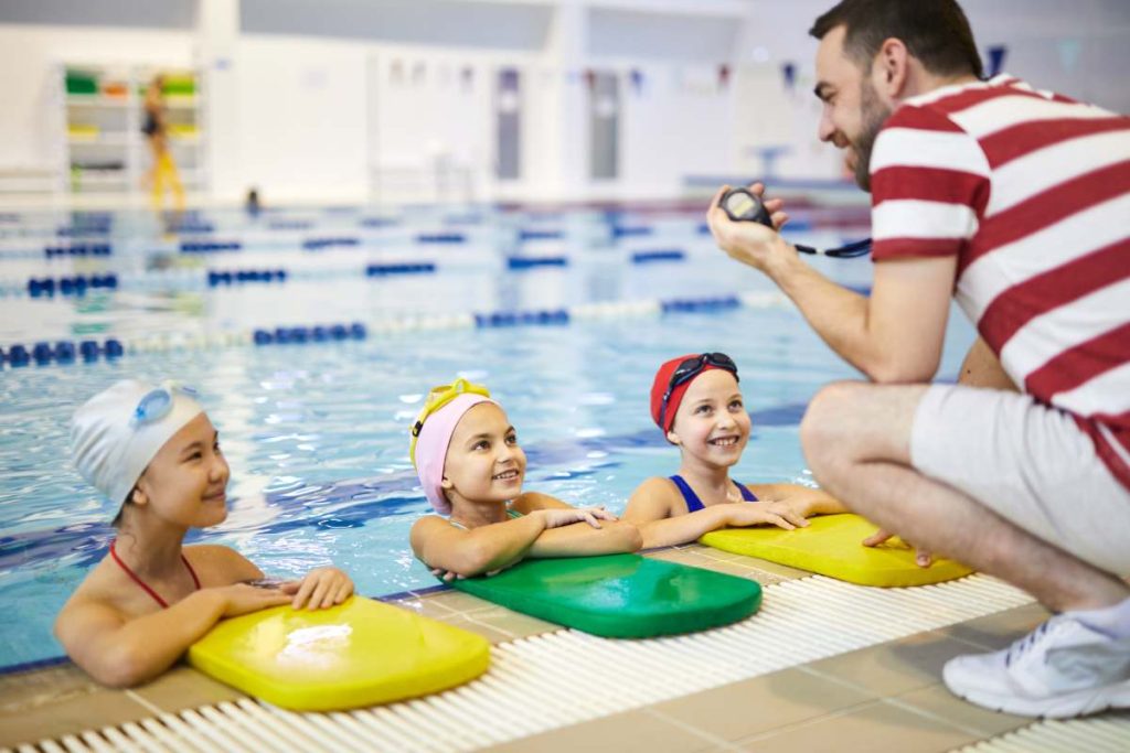 Group of little girls listening to recommendation of the trainer before lesson in the swimming pool