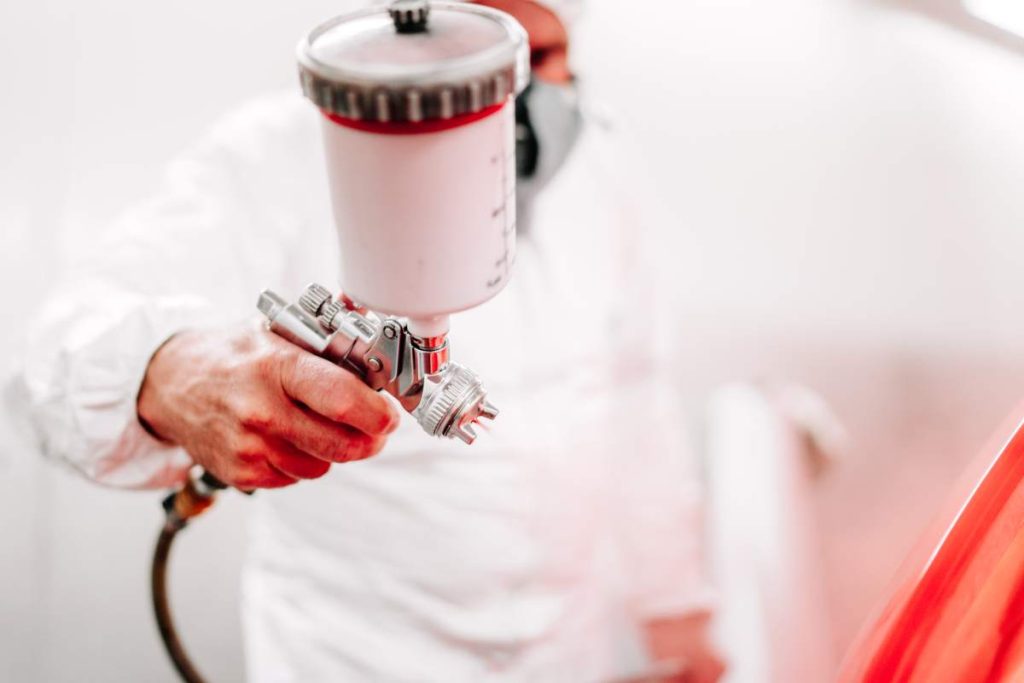 car worker and auto mechanic working and painting a red car using spray gun and compressor