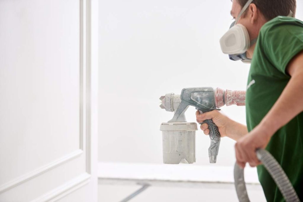 Condtruction worker painting wall with spray gun in white color.