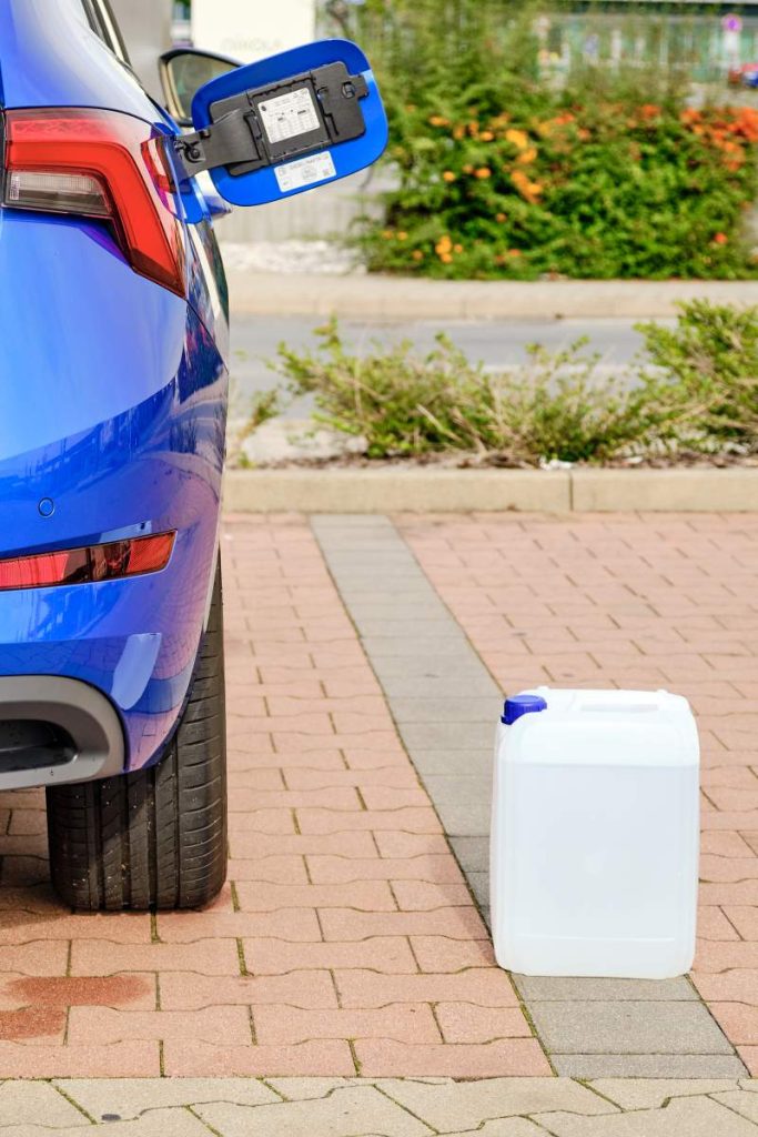 A white canister with a diesel exhaust fluid DEF for reduction of air pollution standing near a blue car