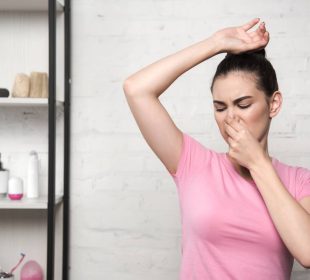 shocked woman plugging nose with hand while looking at underarm