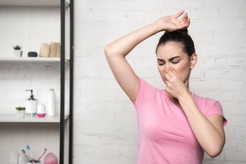 shocked woman plugging nose with hand while looking at underarm