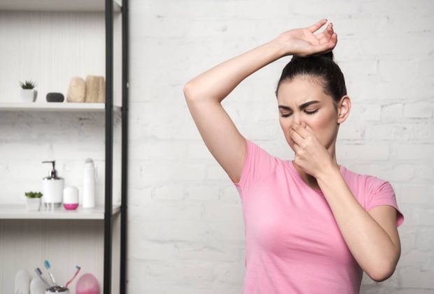 shocked woman plugging nose with hand while looking at underarm