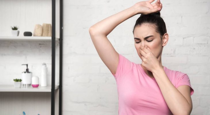 shocked woman plugging nose with hand while looking at underarm