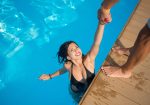 View from above of attractive girl in the swimming pool holding a man's hand trying to get out at resort. Sunny day