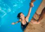 View from above of attractive girl in the swimming pool holding a man's hand trying to get out at resort. Sunny day