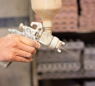 A shallow focus shot of human hands holding a paint sprayer in the workshop